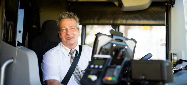 En manlig bussförare som sitter på sin förarstol men vänd mot framdörren. 